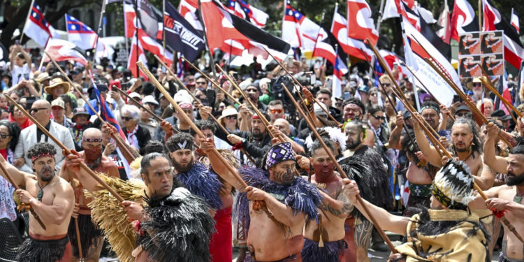 Indigenous Māori people protest outside Parliament against a proposed law that would redefine the country’s founding agreement between Indigenous Māori and the British Crown, in Wellington, New Zealand, Tuesday, Nov. 19, 2024. (AP Photo/Mark Tantrum) 4 of 20 | Thousands of people gather outside New Zealand’s parliament to protest a proposed law that would redefine the country’s founding agreement between Indigenous Māori and the British Crown, in Wellington Tuesday, Nov. 19, 2024. (AP Photo/Mark Tantrum) 5 of 20 | New Zealand’s opposition leader Chris Hipkins, left, does a hongi with Hare Arapere as people gathered outside New Zealand’s parliament to protest a proposed law that would redefine the country’s founding agreement between Indigenous Māori and the British Crown, in Wellington Tuesday, Nov. 19, 2024. (AP Photo/Mark Tantrum) 6 of 20 | Hana-Rāwhiti Maipi-Clarke speaks to the thousands of people gathered outside New Zealand’s parliament to protest a proposed law that would redefine the country’s founding agreement between Indigenous Māori and the British Crown, in Wellington Tuesday, Nov. 19, 2024. (AP Photo/Mark Tantrum) 7 of 20 | Te Haukūnui Hokianga plays a conch shell ahead of a protest at New Zealand’s parliament against a proposed law that would redefine the country’s founding agreement between Indigenous Māori and the British Crown, in Wellington, New Zealand, Tuesday, Nov. 19, 2024. (AP Photo/Mark Tantrum) 8 of 20 | A man carries a child on his shoulders outside New Zealand’s parliament during a protest against a proposed law that would redefine the country’s founding agreement between Indigenous Māori and the British Crown, in Wellington Tuesday, Nov. 19, 2024. (AP Photo/Mark Tantrum) 9 of 20 | Indigenous Māori gather outside Parliament in Wellington, New Zealand, Tuesday, Nov. 19, 2024. (AP Photo/Mark Tantrum) 10 of 20 | Thousands of people gather outside New Zealand’s parliament to protest a proposed law that would redefine the country’s founding agreement between Indigenous Māori and the British Crown, in Wellington Tuesday, Nov. 19, 2024. (AP Photo/Mark Tantrum) 11 of 20 | A petition is delivered to Member of Parliament Rawiri Waititi, left, outside New Zealand’s parliament during a protest against a proposed law that would redefine the country’s founding agreement between Indigenous Māori and the British Crown, in Wellington Tuesday, Nov. 19, 2024. (AP Photo/Mark Tantrum) 12 of 20 | Members of Te Āti Awa, join thousands of people gathered outside New Zealand’s parliament to protest a proposed law that would redefine the country’s founding agreement between Indigenous Māori and the British Crown, in Wellington Tuesday, Nov. 19, 2024. (AP Photo/Mark Tantrum) 13 of 20 | A protester reacts outside New Zealand’s parliament during a demonstration against a proposed law that would redefine the country’s founding agreement between Indigenous Māori and the British Crown, in Wellington Tuesday, Nov. 19, 2024. (AP Photo/Mark Tantrum) 14 of 20 | Indigenous Māori reacts outside New Zealand’s parliament to protest against a proposed law that would redefine the country’s founding agreement between Indigenous Māori and the British Crown, in Wellington, New Zealand, Tuesday, Nov. 19, 2024. (AP Photo/Mark Tantrum) 15 of 20 | Indigenous Māori people walk through the streets of Wellington, New Zealand to protest against a proposed law that would redefine the country’s founding agreement between Indigenous Māori and the British Crown, Tuesday, Nov. 19, 2024. (AP Photo/Mark Tantrum) 16 of 20 | Protesters march carrying placards to New Zealand’s parliament to demonstrate against a proposed law that would redefine the country’s founding agreement between Indigenous Māori and the British Crown, in Wellington, New Zealand, Tuesday, Nov. 19, 2024. (AP Photo/Mark Tantrum) 17 of 20 | ACT Party leader David Seymour, center, looks on as thousands of people gather outside New Zealand’s parliament to protest a proposed law that would redefine the country’s founding agreement between Indigenous Māori and the British Crown, in Wellington Tuesday, Nov. 19, 2024. (AP Photo/Mark Tantrum) 18 of 20 | Thousands of people gather outside New Zealand’s parliament to protest a proposed law that would redefine the country’s founding agreement between Indigenous Māori and the British Crown, in Wellington Tuesday, Nov. 19, 2024. (AP Photo/Mark Tantrum) 19 of 20 | Thousands of people gather outside New Zealand’s parliament to protest a proposed law that would redefine the country’s founding agreement between Indigenous Māori and the British Crown, in Wellington Tuesday, Nov. 19, 2024. (AP Photo/Mark Tantrum) 20 of 20 | Thousands of people gather outside New Zealand’s parliament to protest a proposed law that would redefine the country’s founding agreement between Indigenous Māori and the British Crown, in Wellington Tuesday, Nov. 19, 2024. (AP Photo/Charlotte Graham-McLay) By CHARLOTTE GRAHAM-McLAY Updated 10:38 AM GMT+6, November 19, 2024 WELLINGTON, New Zealand (AP) — As tens of thousands of marchers crowded the streets in New Zealand’s capital Wellington on Tuesday, the throng of people, flags aloft, had the air of a festival or a parade rather than a protest. They arrived to oppose a law that would reshape the county’s founding treaty between Indigenous Māori and the British Crown. But for many, it was about something more: a celebration of a resurging Indigenous language and identity that colonization had once almost destroyed. “Just fighting for the rights that our tūpuna, our ancestors, fought for,” Shanell Bob said as she waited for the march to begin. “We’re fighting for our tamariki, for our mokopuna, so they can have what we haven’t been able to have,” she added, using the Māori words for children and grandchildren. What was likely the country’s largest-ever protest in support of Māori rights — a subject that has preoccupied modern New Zealand for much of its young history — followed a long tradition of peaceful marches the length of the country that have marked turning points in the history of modern New Zealand. Advertisement “We’re going for a walk!” One organizer proclaimed from the stage as crowds gathered at the opposite end of the city from the nation’s Parliament. Some had traveled the length of the country over the past nine days. Related Stories fowave Lawmakers stage Māori protest in New Zealand's parliament fowave New Zealand's founding treaty is at a flashpoint. Why are thousands protesting for Māori rights? fowave New Zealand PM apologizes to survivors of abuse in state and church care For many, the turnout reflected growing solidarity on Indigenous rights from non-Māori. At bus stops during the usual morning commute, people of all ages and races waited with Māori sovereignty flags. Some local schools said they would not register students as absent. The city’s mayor joined the protest. The bill that marchers were opposing is unpopular and unlikely to become law. But opposition to it has exploded, which marchers said indicated rising knowledge of the Treaty of Waitangi’s promises to Māori among New Zealanders — and a small but vocal backlash from those who are angered by attempts by courts and lawmakers to keep them. Advertisement Māori marching for their rights as outlined in the treaty is not new. But the crowds were larger than at treaty marches before and mood was changed, Indigenous people said. “It’s different to when I was a child,” Bob said. “We’re stronger now, our tamariki are stronger now, they know who they are, they’re proud of who they are.” As the marchers moved through the streets of Wellington with ringing Māori haka — rhythmic chants — and waiata, or songs, thousands more holding signs lined the pavement in support. Some placards bore jokes or insults about the lawmakers responsible for the bill, which would change the meaning of the principles of the 1840 Treaty of Waitangi and prevent them from applying only to Māori — whose chiefs signed the document when New Zealand was colonized. But others read “proud to be Māori” or acknowledged the bearer’s heritage as a non-Māori person endorsing the protest. Some denounced the widespread expropriation of Māori land during colonization, one of the main grievances arising from the treaty. “The treaty is a document that lets us be here in Aotearoa so holding it up and respecting it is really important,” said Ben Ogilvie, who is of Pākehā or New Zealand European descent, using the Māori name for the country. “I hate what this government is doing to tear it down.” Advertisement Police said 42,000 people tried to crowd into Parliament’s grounds, with some spilling into the surrounding streets. People crammed themselves onto the children’s slide on the lawn for a vantage point; others perched in trees. The tone was almost joyful; as people waited to leave the cramped area, some struck up Māori songs that most New Zealanders learn at school. A sea of Māori sovereignty flags in red, black and white stretched down the lawn and into the streets. But marchers bore Samoan, Tongan, Indigenous Australian, U.S., Palestinian and Israeli flags, too. At Parliament, speeches from political leaders drew attention to the reason for the protest — a proposed law that would change the meaning of words in the country’s founding treaty, cement them in law and extend them to everyone. Advertisement Its author, libertarian lawmaker David Seymour — who is Māori — says the process of redress for decades of Crown breaches of its treaty with Māori has created special treatment for Indigenous people, which he opposes. The bill’s detractors say it would spell constitutional upheaval, dilute Indigenous rights, and has provoked divisive rhetoric about Māori — who are still disadvantaged on almost every social and economic metric, despite attempts by the courts and lawmakers in recent decades to rectify inequities caused in large part by breaches of the treaty. It is not expected to ever become law, but Seymour made a political deal that saw it shepherded through a first vote last Thursday. In a statement Tuesday, he said the public could now make submissions on the bill — which he hopes will reverse in popularity and experience a swell of support. Advertisement Seymour briefly walked out onto Parliament’s forecourt to observe the protest, although he was not among the lawmakers invited to speak. Some in the crowd booed him. The protest was “a long time coming,” said Papa Heta, one of the marchers, who said Māori sought acknowledgement and respect. “We hope that we can unite with our Pākehā friends, Europeans,” he added. “Unfortunately there are those that make decisions that put us in a difficult place.” CHARLOTTE GRAHAM-McLAY Graham-McLay is an Associated Press reporter covering regional and national stories about New Zealand, Australia and the Pacific Islands by putting them in a global context. She is based in Wellington. twitter mailto by Taboola Suggested For You Asia-Pacific summit closes in Peru with China’s Xi front and center as Trump whiplash looms The best IPO stock pick of 2016? The Motley Fool: Advertisement In a meeting with Biden, China's Xi cautions US to 'make the wise choice' to keep relations stable Operation False Target: How Russia plotted to mix a deadly new weapon among decoy drones in Ukraine Latest typhoon lashes the Philippines, causing tidal surges and displacing massive numbers of people An Australian on trial for drugs in Japan says she's the victim of a romance scamAn Australian accused of smuggling amphetamines in a suitcase has appeared in a Japanese court nearly two years after her arrest and said she was tricked into carrying them as part of an online romance scam.AP News AP News Quiz - Nov. 18, 2024Test your news knowledge with the daily quick quiz. The faster you answer the five questions, the higher your score will be.AP News Crossout 2.0: SuperchargedCrossout Advertisement: Play Now This house is only 27 sq. ft. but when you see the inside you'll want it!Tips and Tricks Advertisement: Your Package Delivered Anywhere [Read More]softafrique Advertisement: Contact Us We Deliver to Your Doorstep [Learn More]softafrique Advertisement: Contact Us Halloween Vibes With Candy Corn, Cheerleader Camp, Crackcoon, and Creepy Classicsbwpodcast.com Advertisement: New Insurance Plans for Sarulia (Learn More)top10insurance Advertisement: Click Here Easy Insurance at an Attractive Price (Sign Up)Get the top insurance choices for millennials at a price you'll love. Explore now.top10insurance Advertisement: Click Here Smart Size will change how you shopProper Cloth Advertisement: A perfect fitting shirt for anyone?Proper Cloth Advertisement: This Insurance Actually Works (Check It Out)top10insurance Advertisement: Click Here top 10 health insurance companies in uae TOP 10 INSURANCEtop10insurance Advertisement: Click Here A rare Israeli strike on central Beirut kills Hezbollah's spokesman, official saysAn official, who spoke on condition of anonymity because they were not authorized to brief the media, said Mohammed Afif was killed in the strike on Sunday.AP News PHOTO COLLECTION: Mike Tyson vs Jake PaulThis is a collection of photos chosen by AP photo editors.AP News Buy a perfect fitting shirt easilyProper Cloth Advertisement: The shirt company disrupting retailProper Cloth Advertisement: Buying custom shirts just got easyProper Cloth Advertisement: Victoria Kjær Theilvig of Denmark is crowned the 73rd Miss UniverseKjaer, an animal protection advocate who works in the diamond selling business, beat out Miss Nigeria at the end of 73rd edition of the competition in Mexico City.AP News A gold pocket watch given to the captain who rescued Titanic survivors sells for a record priceA gold pocket watch given to the ship captain who rescued 700 survivors from the Titanic has sold at auction for nearly $2 million.AP News Investigation reveals a Russian factory's plan to mix decoys with a new deadly weapon in Ukraine Israeli troops reach deepest point in Lebanon since Oct. 1 invasion, Lebanese media say Gabbard's sympathetic views toward Russia cause alarm as Trump's pick to lead intelligence services Advertisement