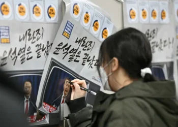A woman writes on a poster showing South Korea President Yoon Suk Yeol, with text that reads 'insurrection criminal Yoon is over' (ANTHONY WALLACE) (ANTHONY WALLACE/AFP/AFP)